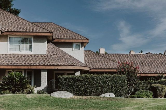 Suburban house with red tile roof, hedge, and green lawn under cloudy sky