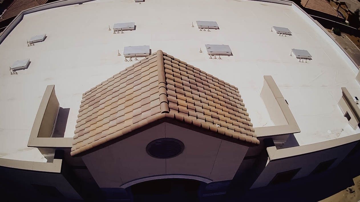 Aerial view of a beige building roof with a central brown-tiled peak and a round window below.