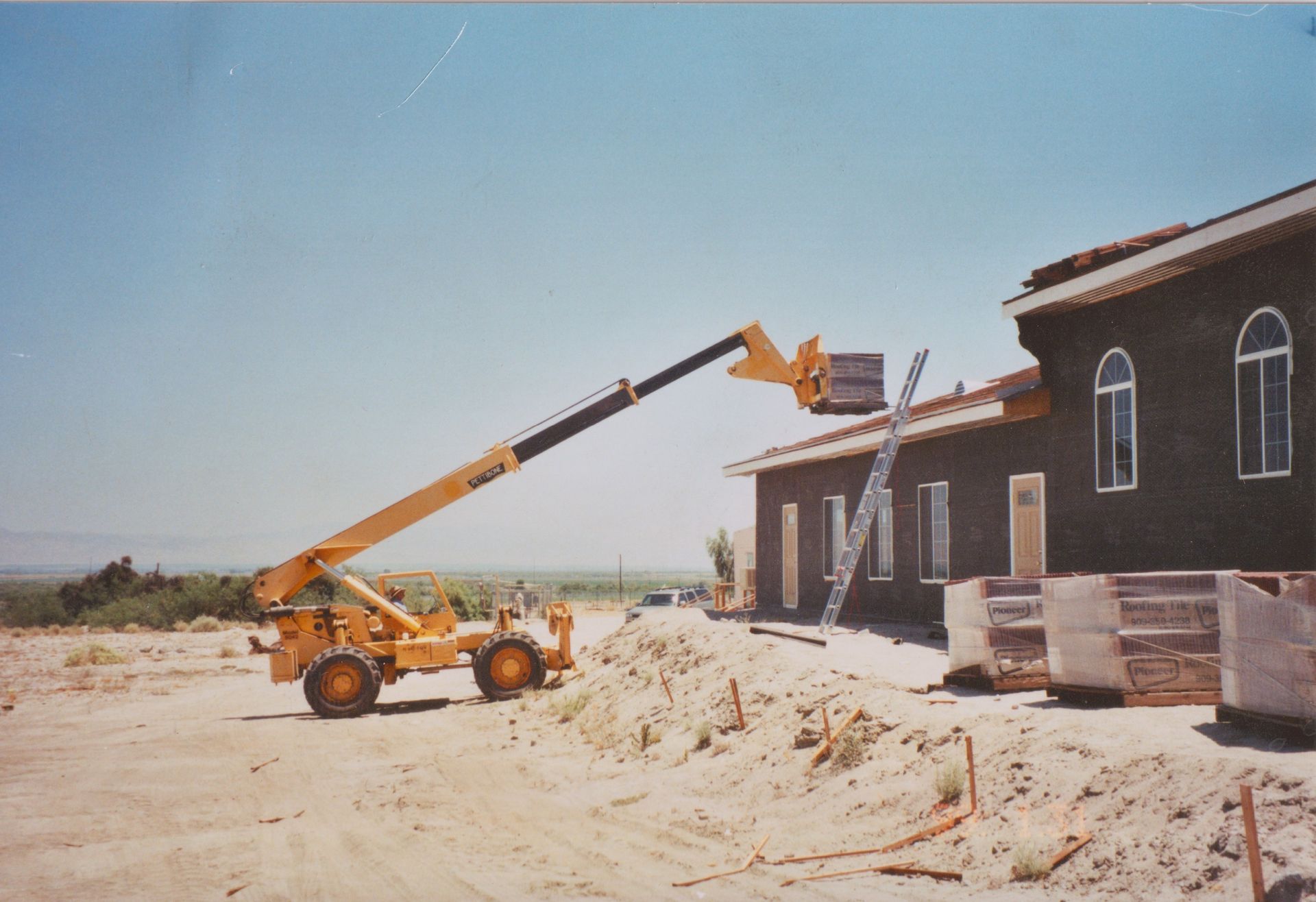 Construction site with yellow forklift lifting materials beside a dark building under construction