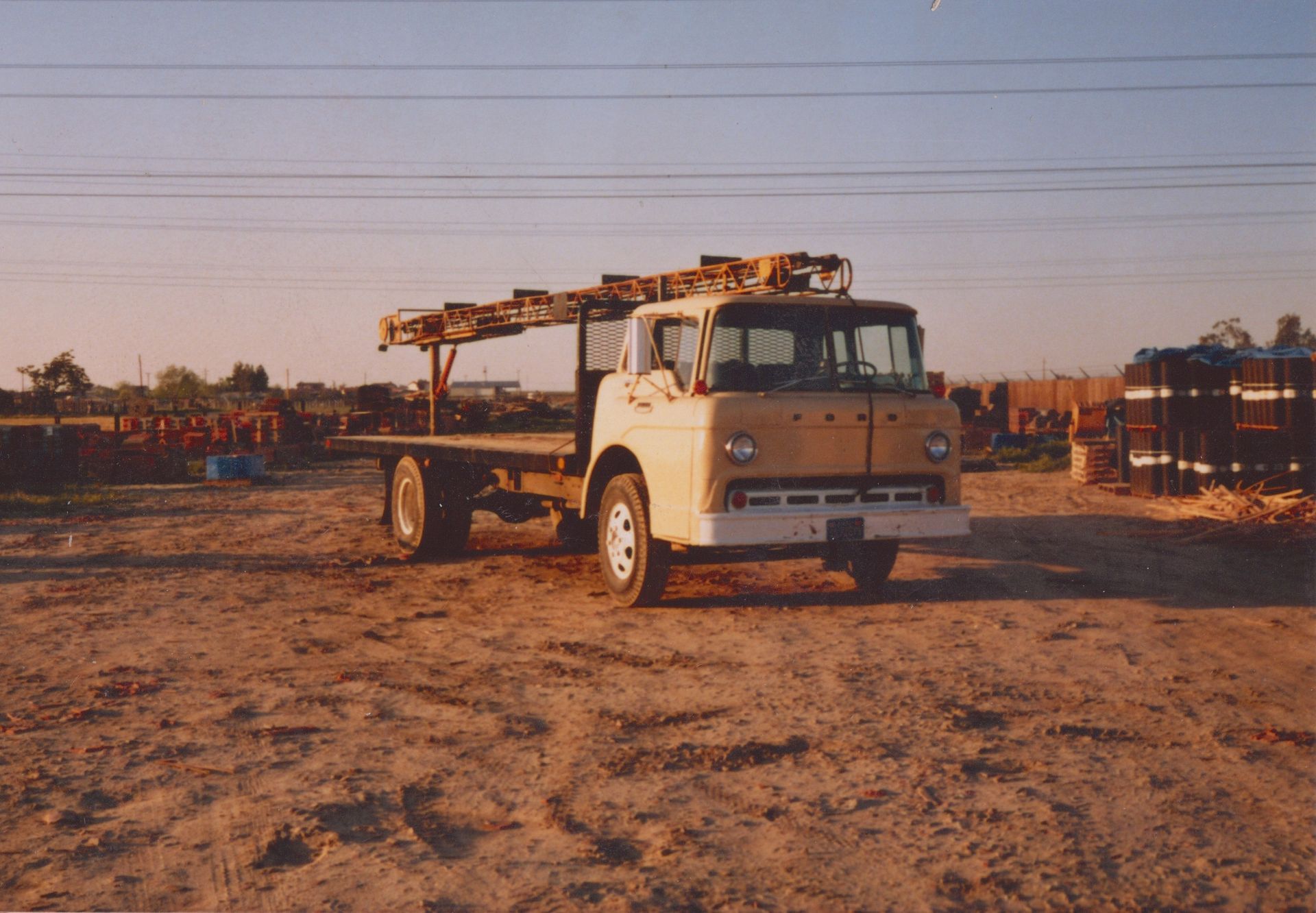 White flatbed truck parked on a dusty lot at sunset with long shadows and power lines overhead