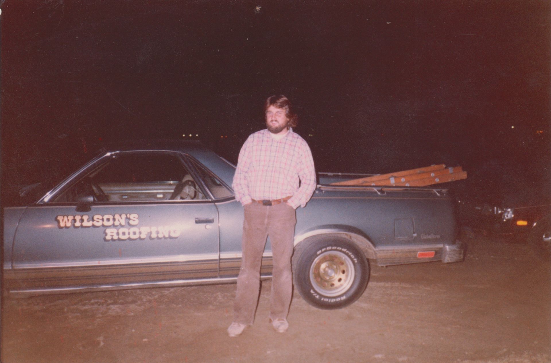 Person standing beside a blue pickup truck at night, with “WILSON’S” painted on the door.