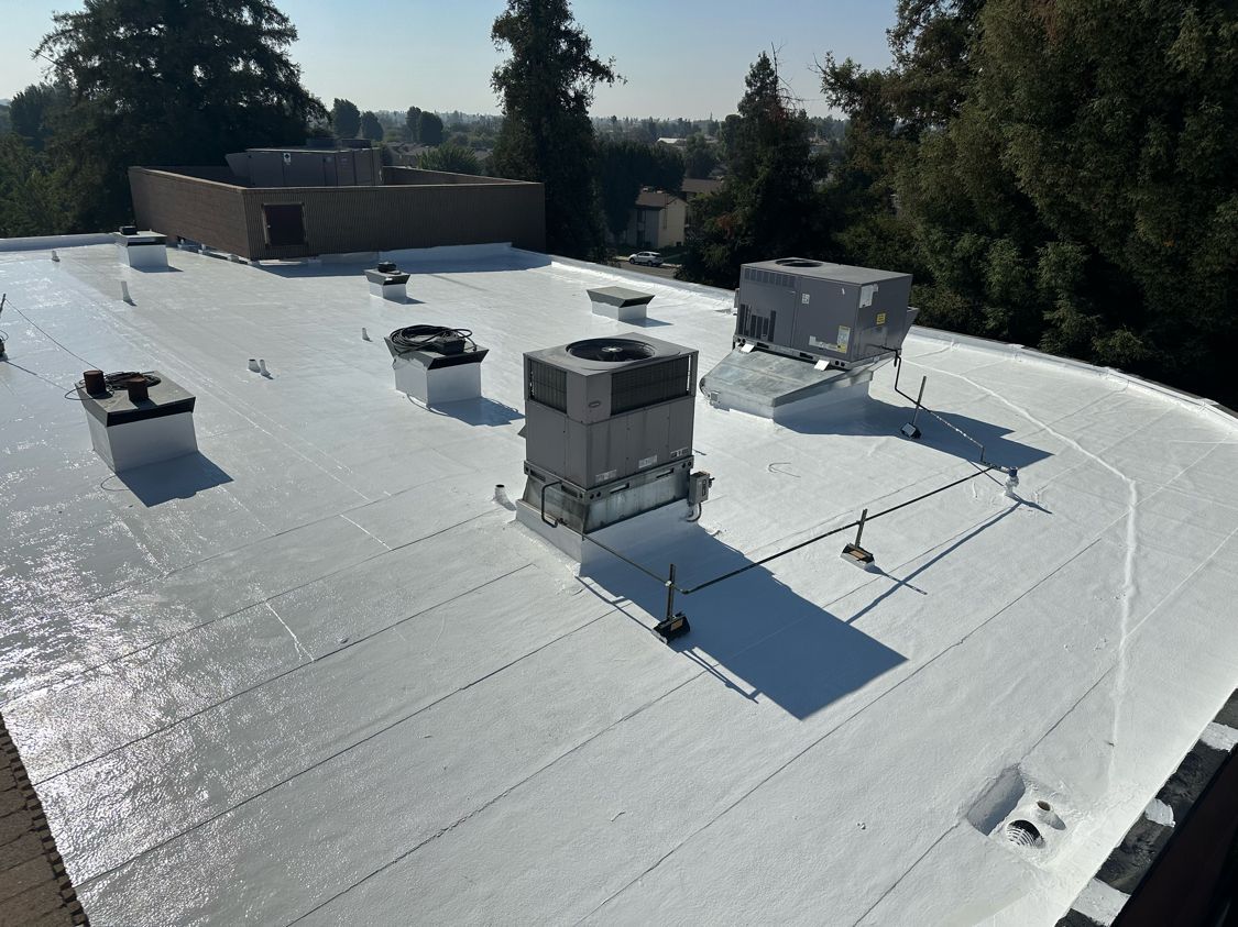 Rooftop with white membrane surface and several HVAC units in bright sunlight