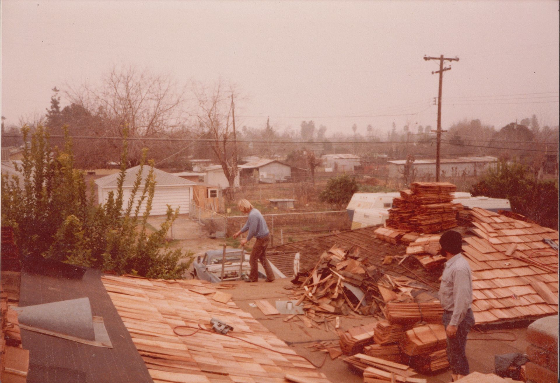 Workers repair a roof amid storm damage in a hazy neighborhood.