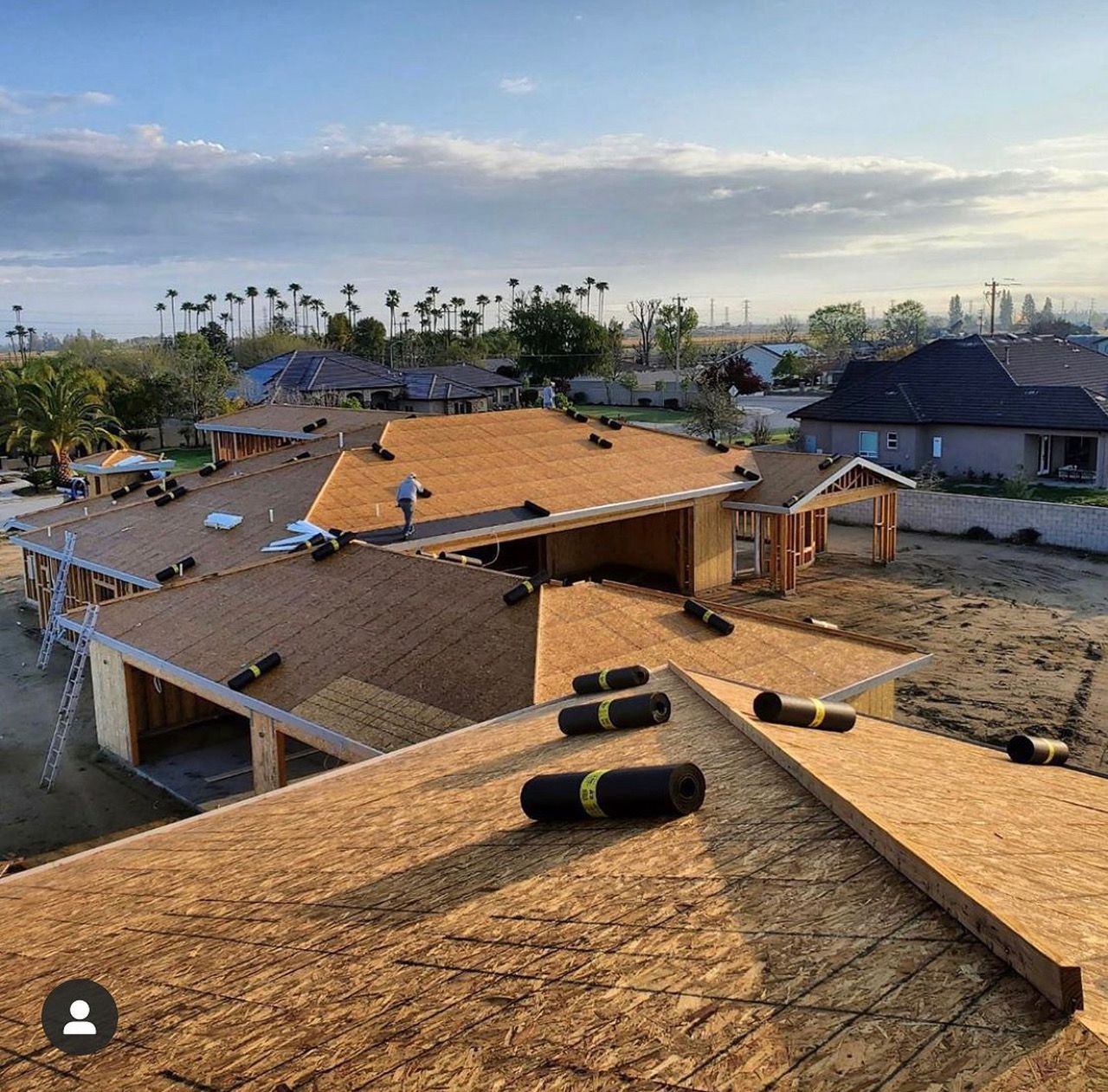 Partially roofed homes under construction in a neighborhood after storm damage, with shingles in foreground