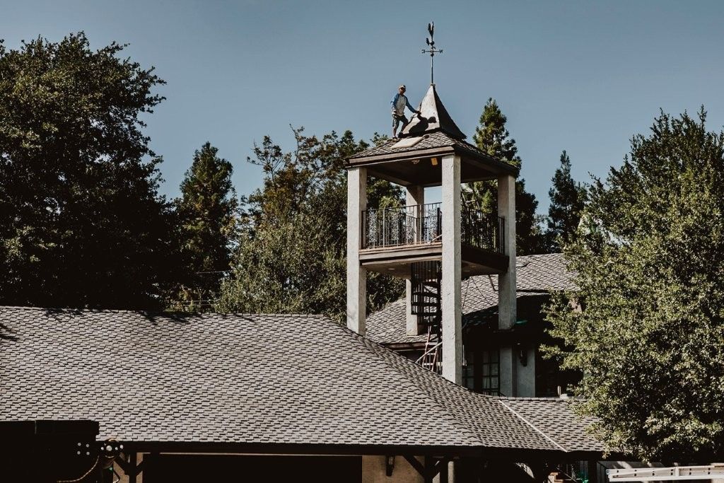 Rooftop with a small white tower and bird sculptures against a clear sky, surrounded by trees