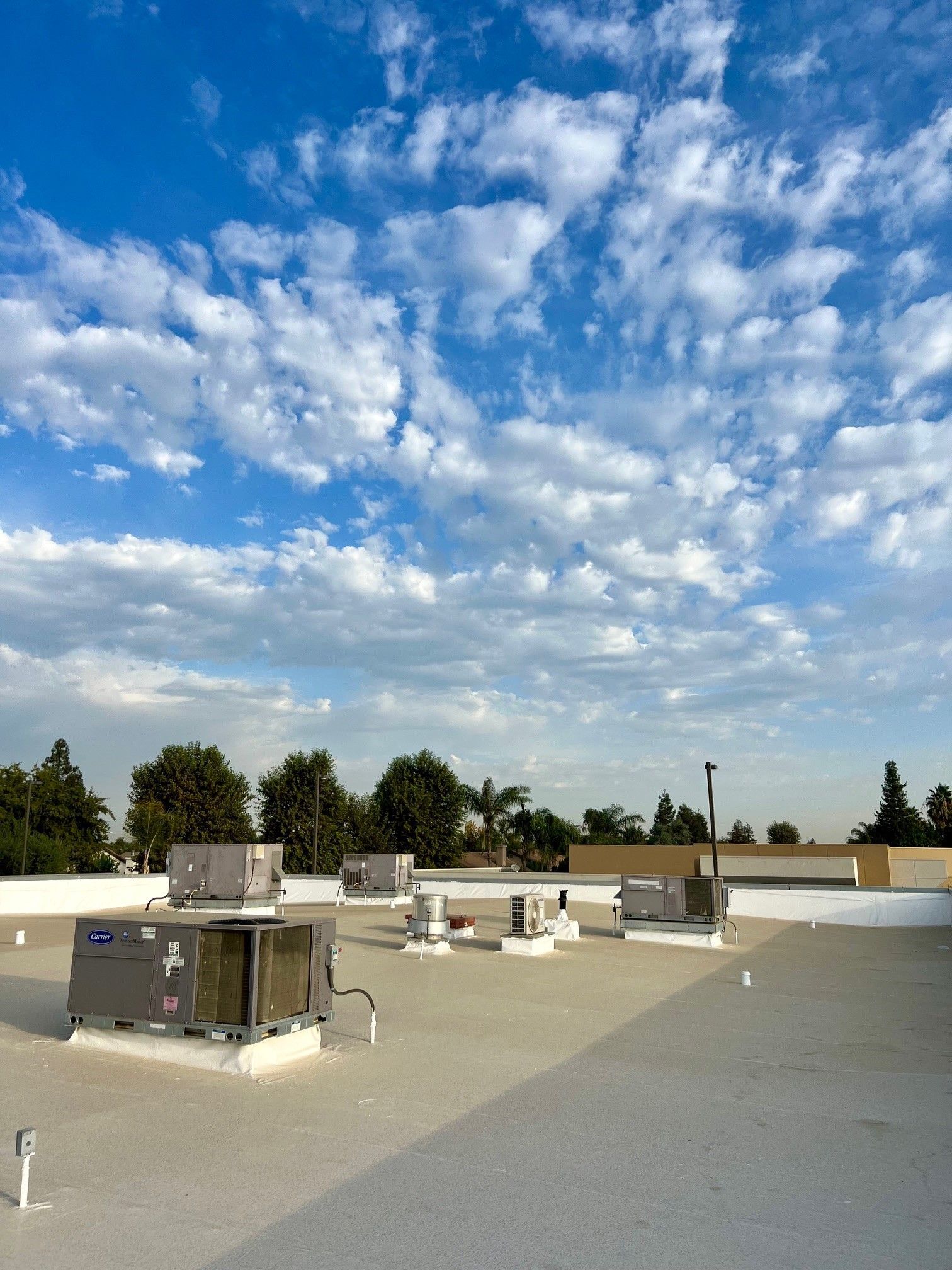 Rooftop with HVAC units under a blue sky with scattered clouds