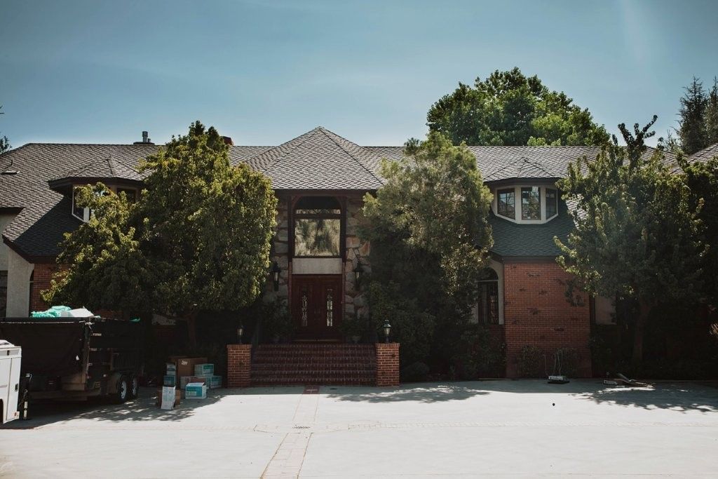 Suburban house with brick facade, tiled roof, and trees in front under a bright sky