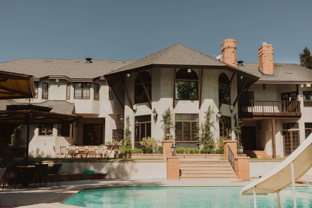 Luxury villa with a tiled roof and central pool, featuring balconies, pillars, and stone steps.