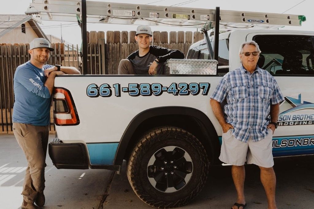 Three workers posing beside a white utility truck with ladders and a visible phone number.