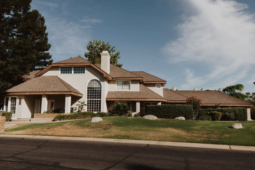 Large stucco house with tile roof, arched windows, and a long driveway under a clear sky