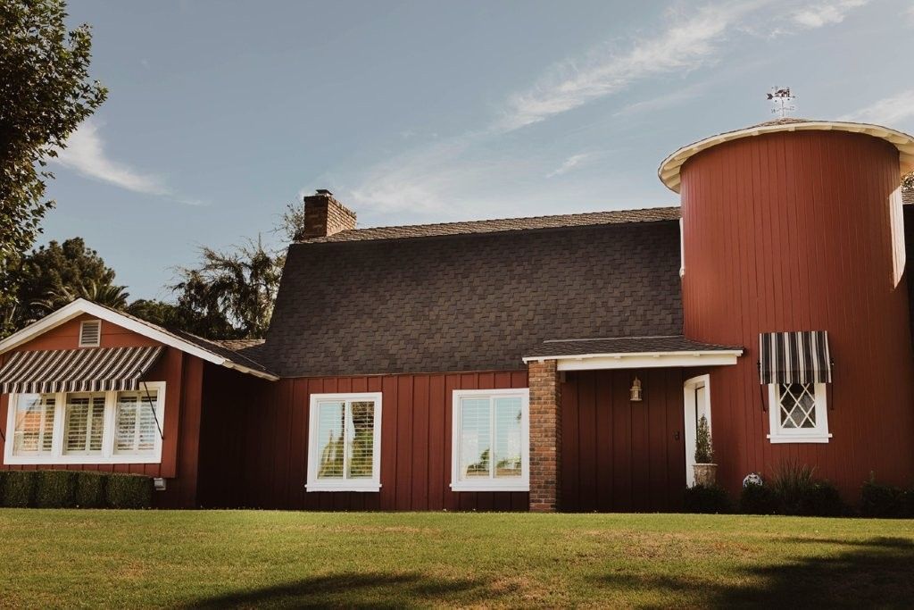 Red farmhouse with a thatched roof and a round turret, set on a grassy lawn under a blue sky