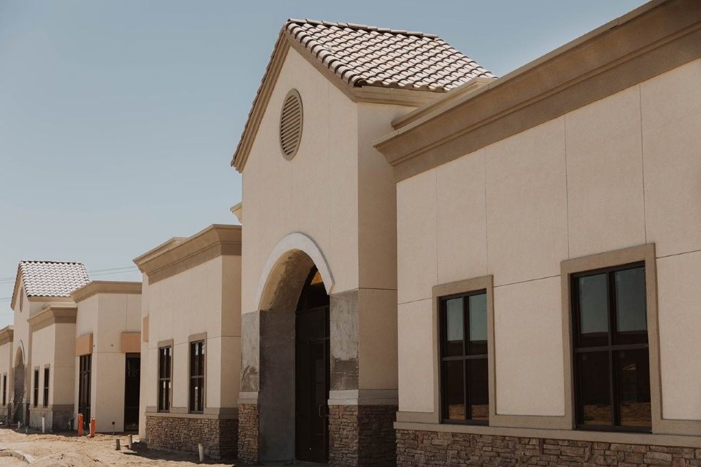 Row of beige stucco buildings with arched entrances and tiled roofs in bright sunlight