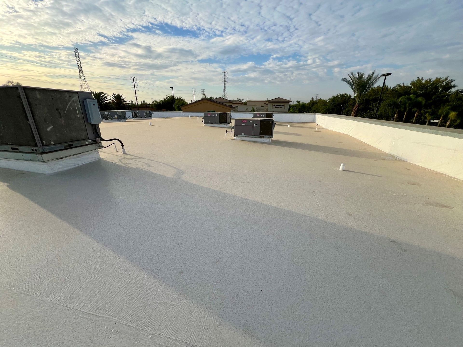 Rooftop with white waterproof coating, HVAC units, and a cloudy sky at sunset