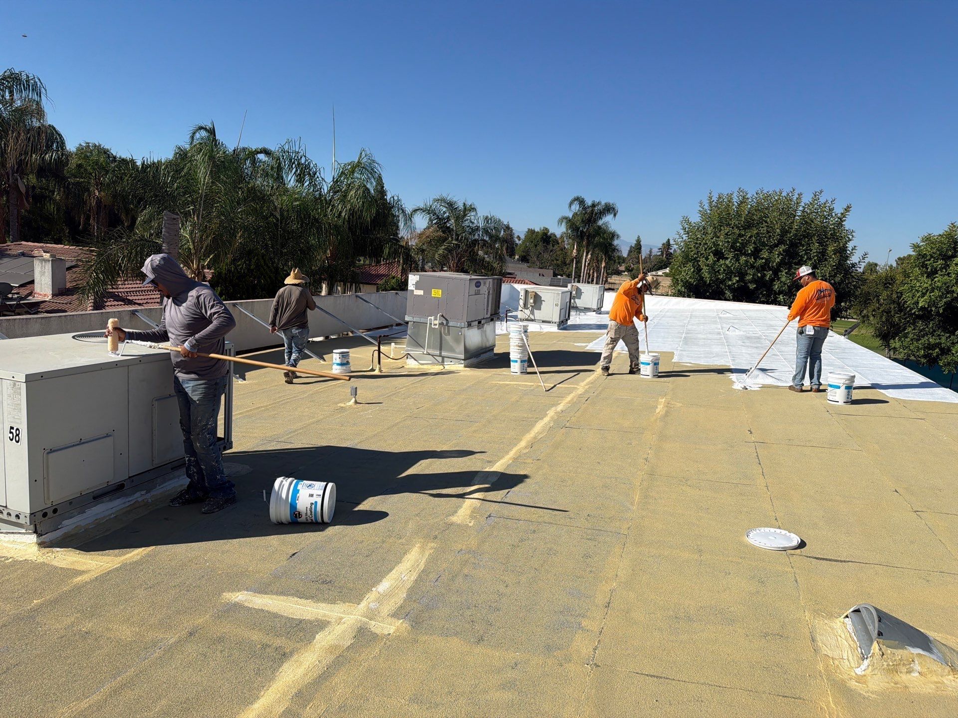 Workers installing rooftop insulation under a clear blue sky