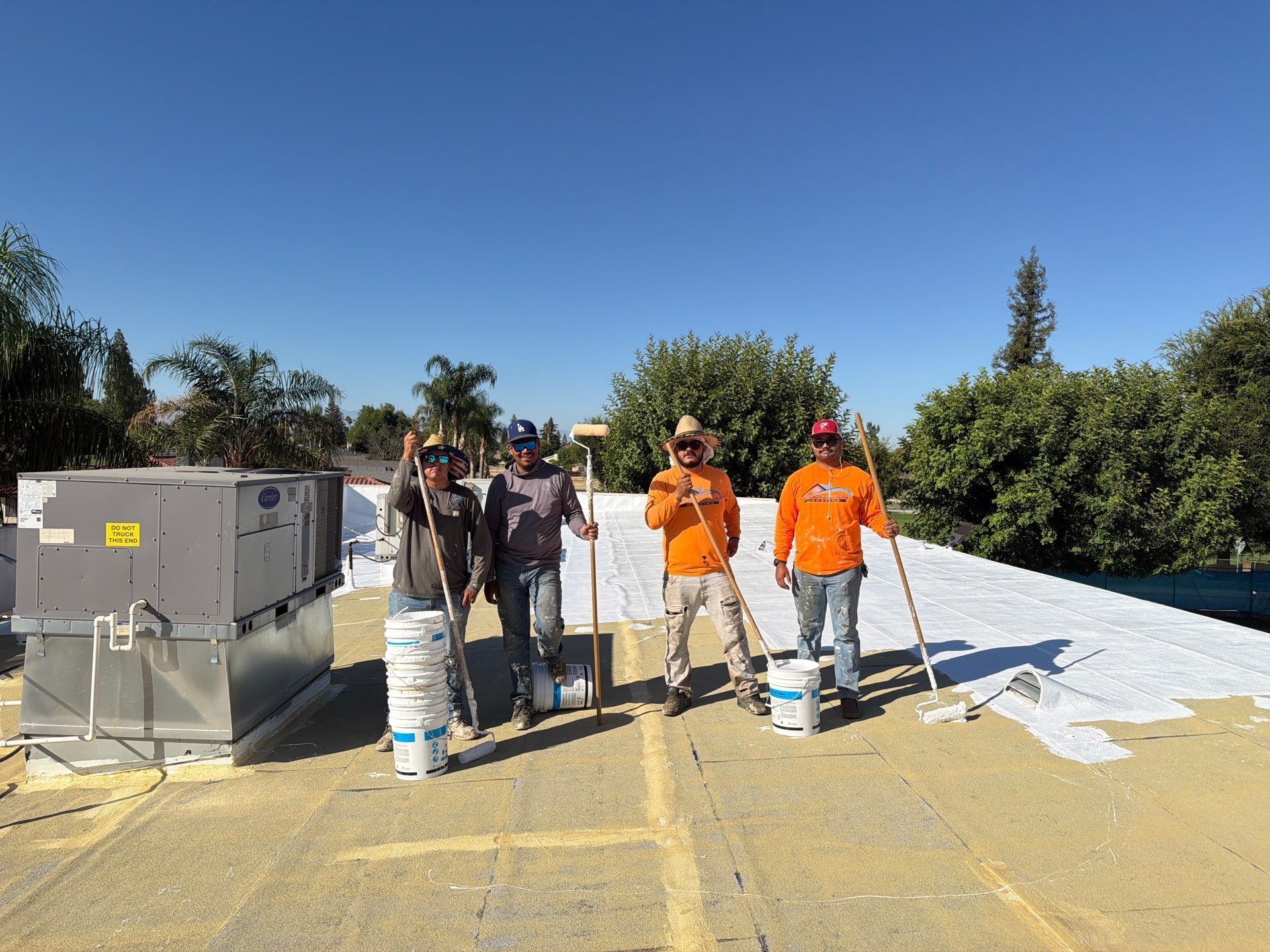 Workers in orange shirts and hats on a rooftop beside equipment under a clear blue sky