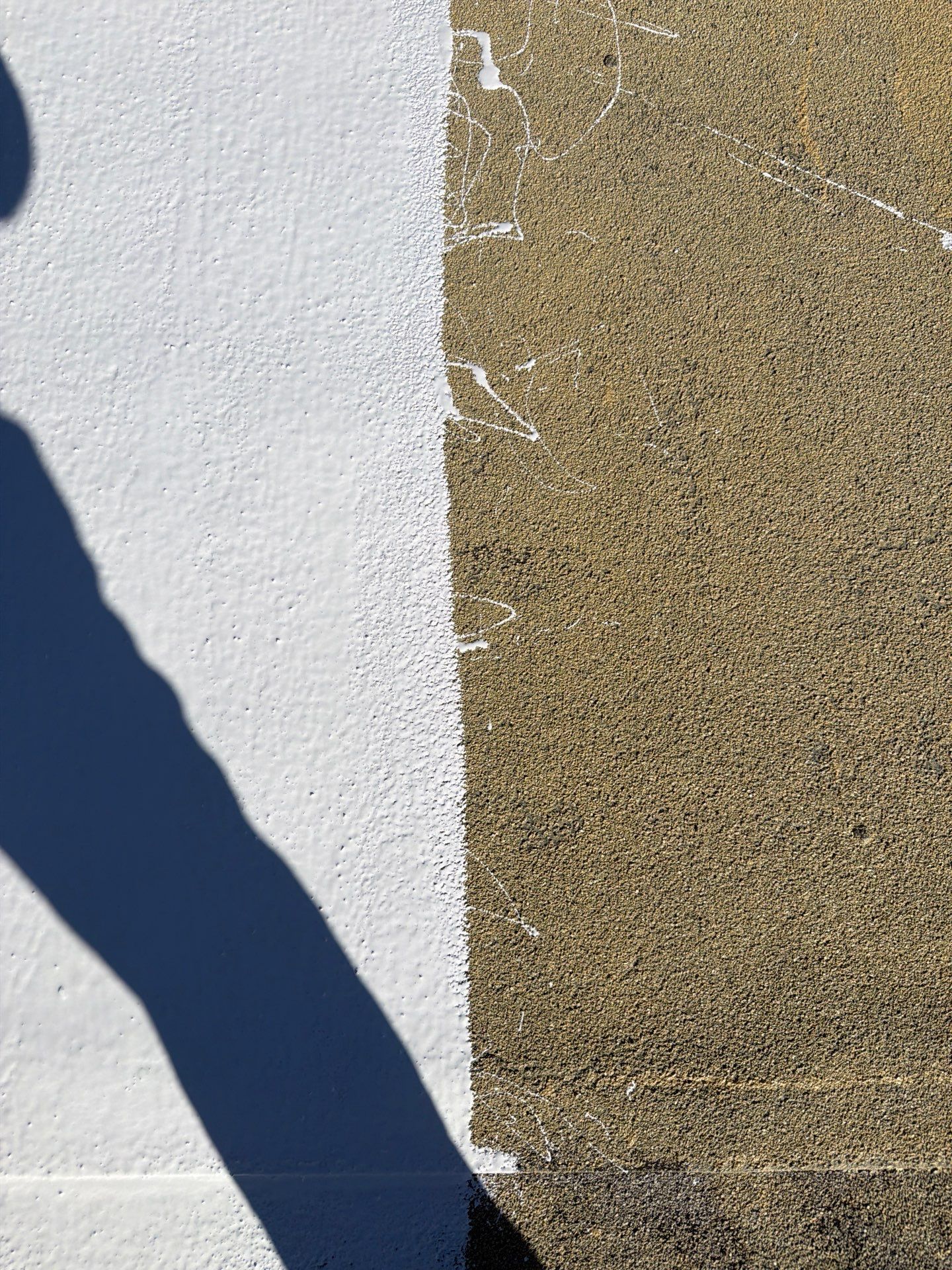 Close-up of a white stucco wall meeting a tan textured surface with a dark diagonal shadow.