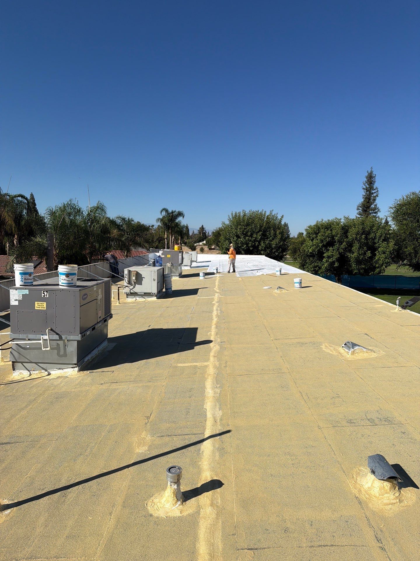 Flat rooftop under construction with white underlayment, HVAC units, and blue sky.