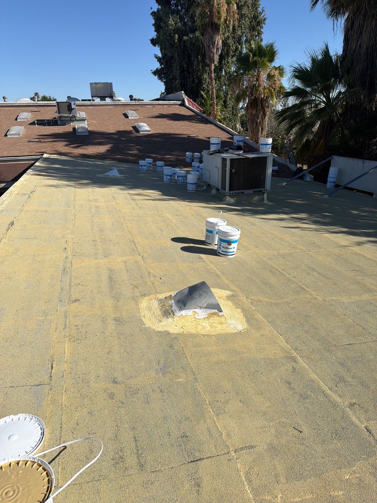 Flat roof with yellow waterproofing, vents, and rooftop equipment under a clear sky