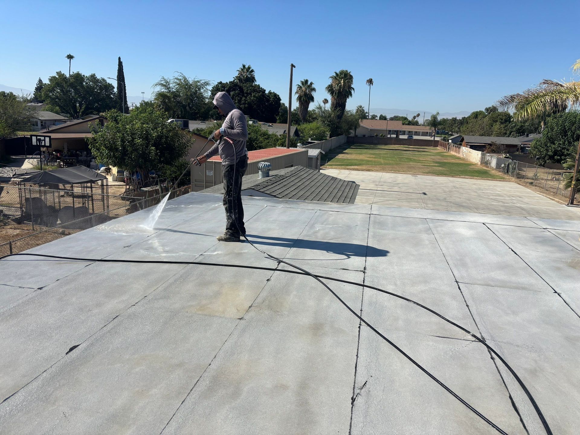 Worker spraying concrete on a driveway in a sunny residential yard