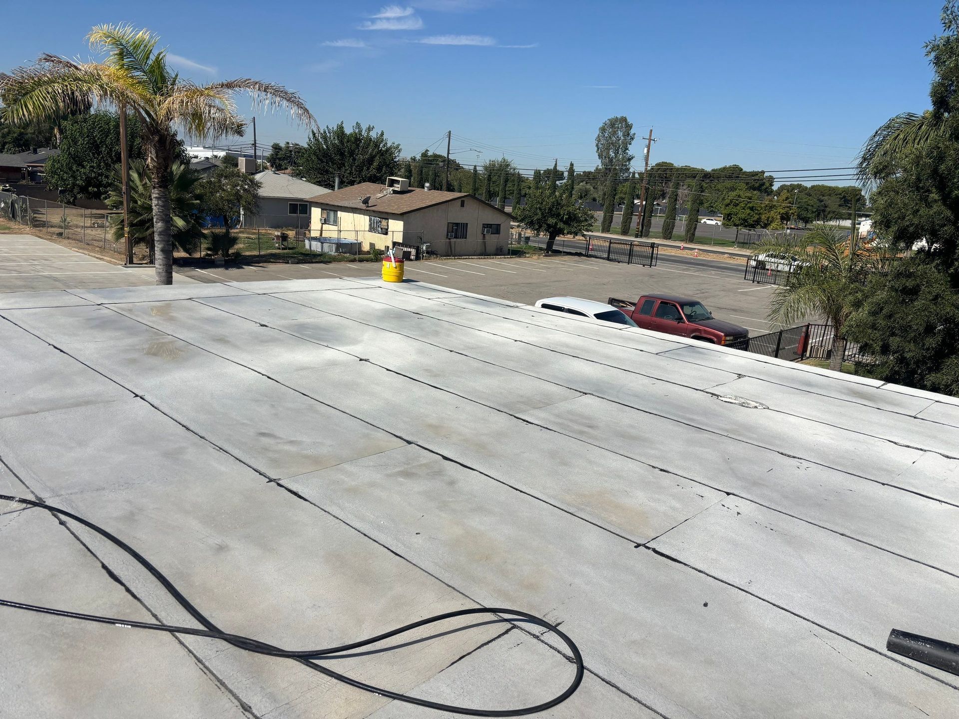Rooftop with white panels and cables overlooking trees, houses, and parked cars under a clear blue sky