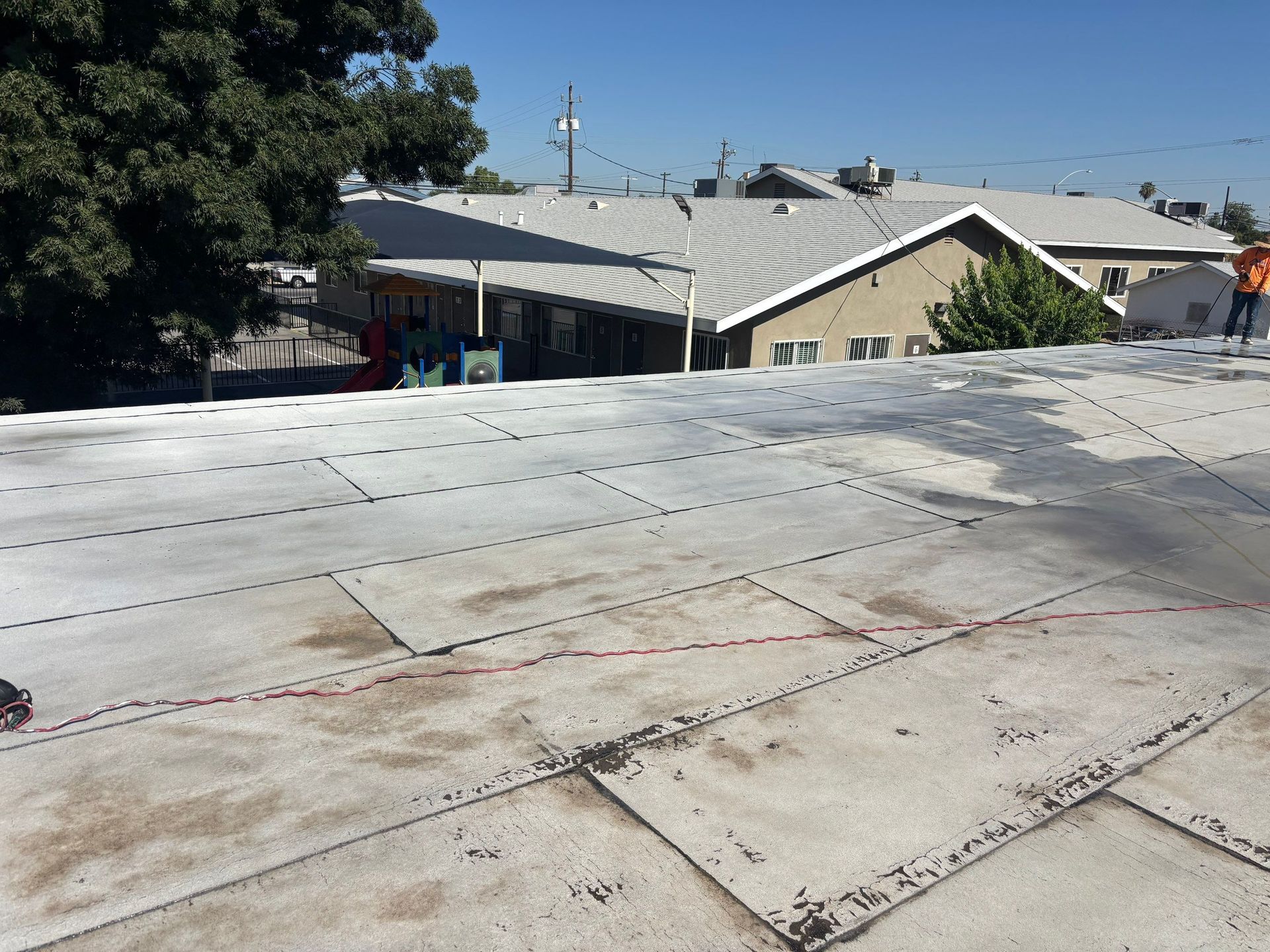 Flat white rooftop overlooking beige buildings and trees under a clear blue sky