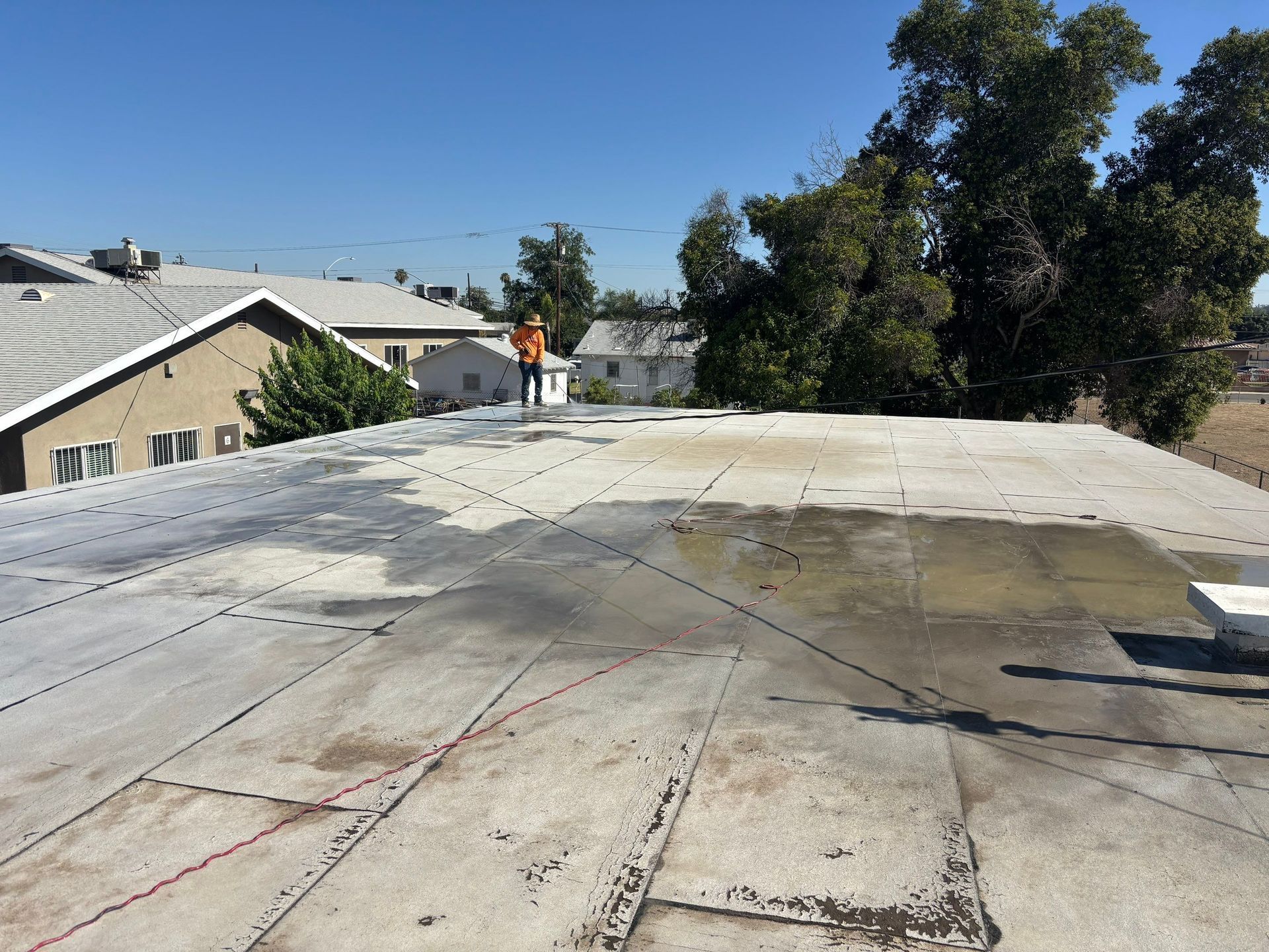 Flat rooftop with water stains, neighboring houses, and trees under a clear blue sky