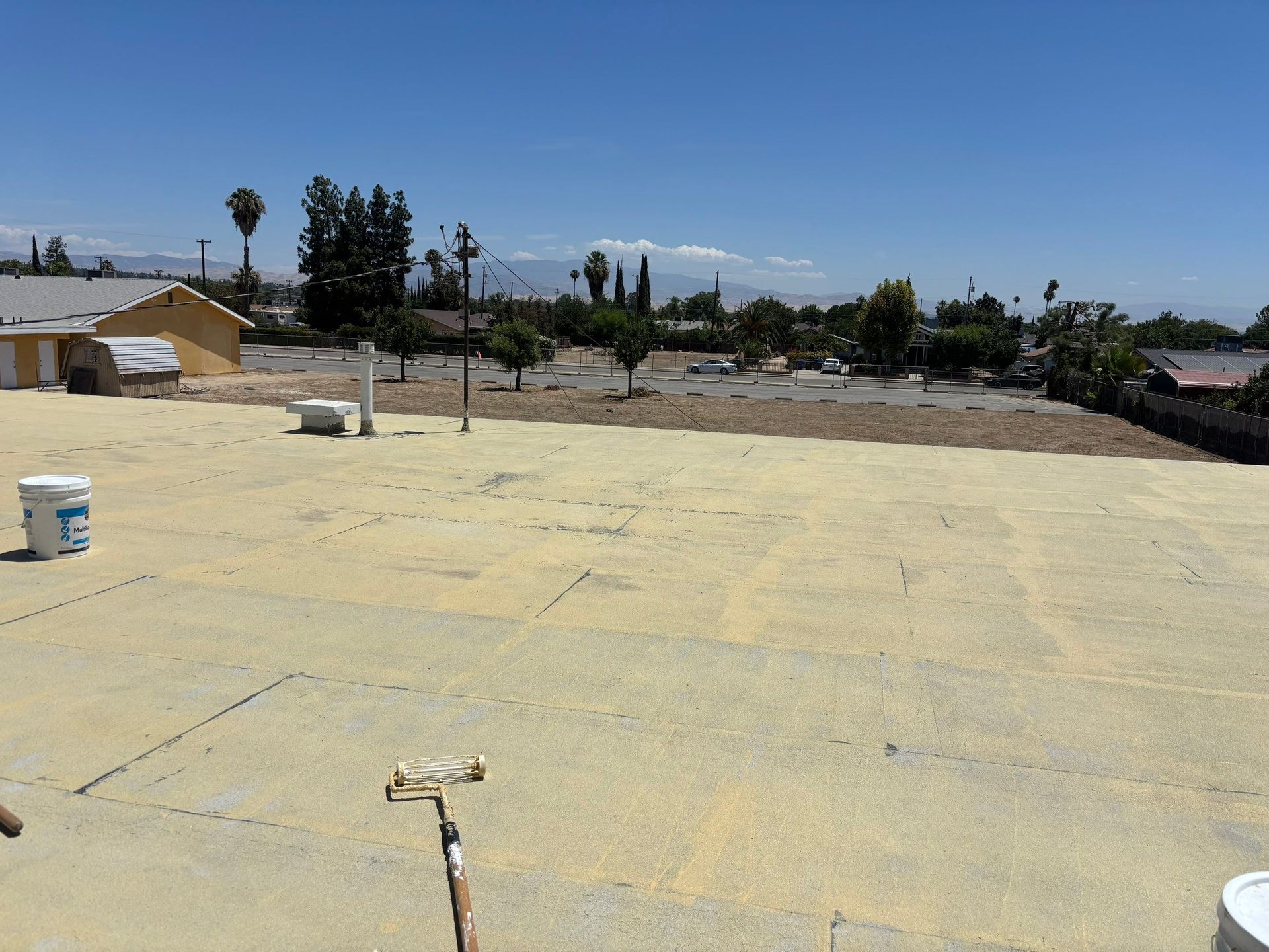 Bare dirt lot beside a large concrete slab under a clear blue sky, with trees and houses in the distance
