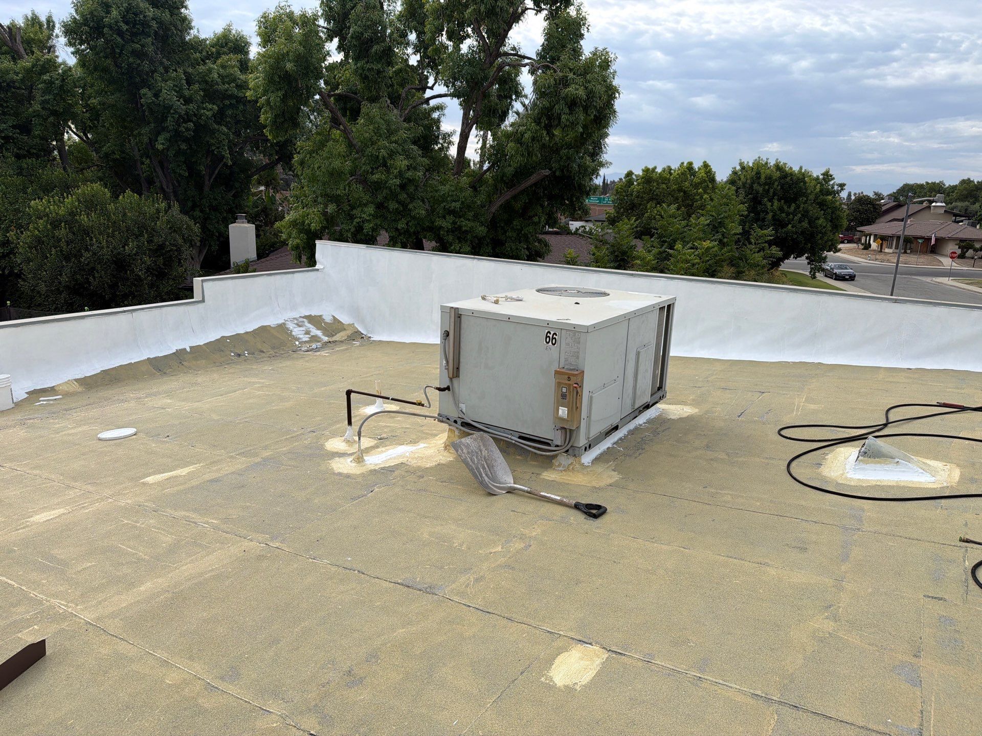 Rooftop with white walls, gravel surface, and an HVAC unit near trees and houses in the distance