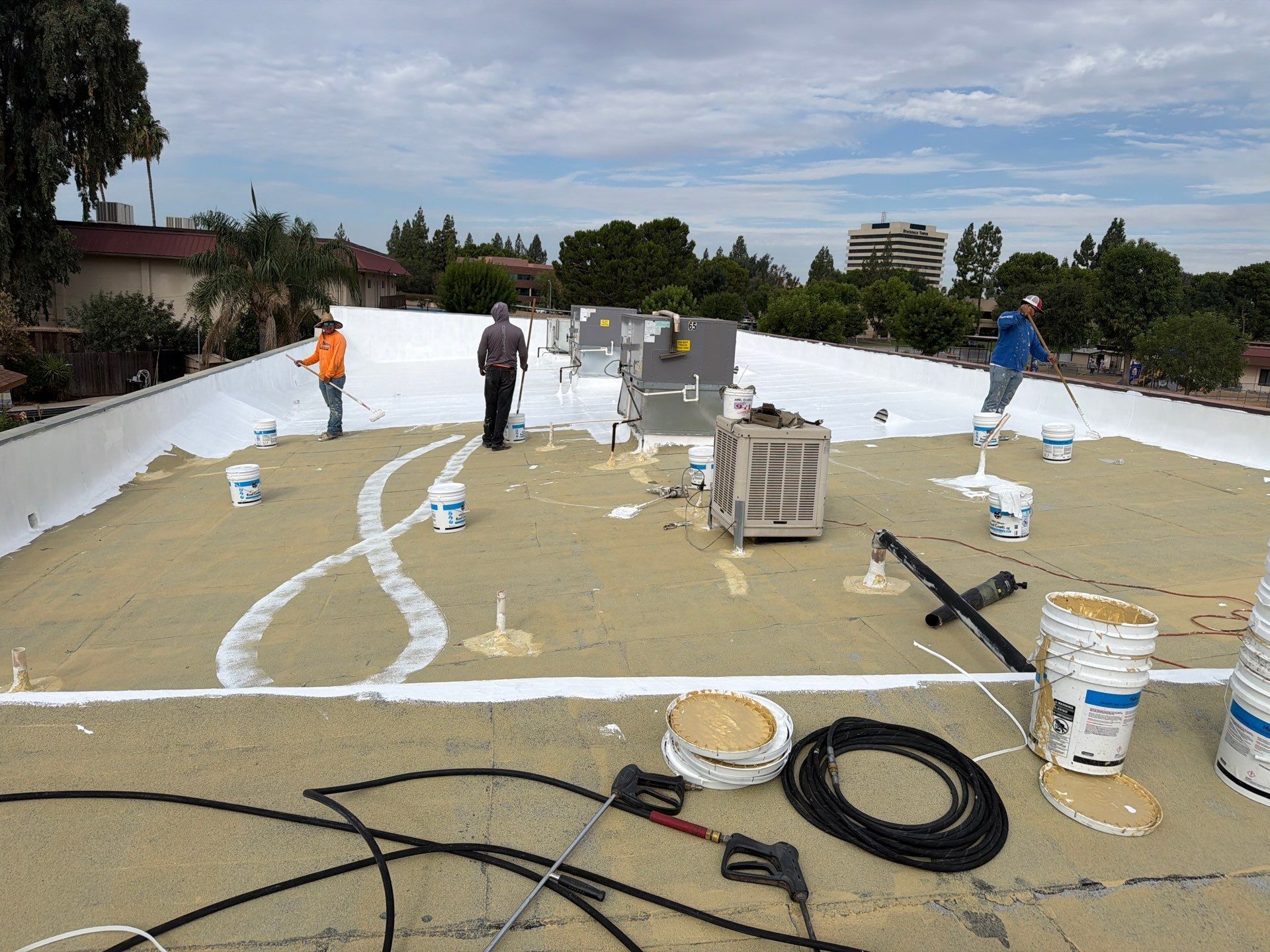 Workers painting a large white rooftop with buckets, hoses, and tools spread across the surface.