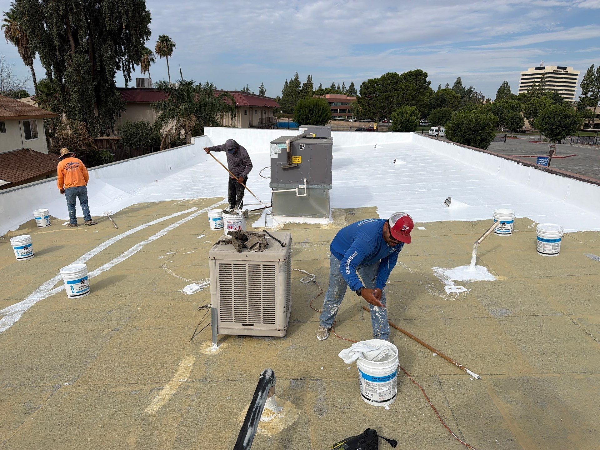 Workers painting a large white roof with buckets and tools on a sunny day
