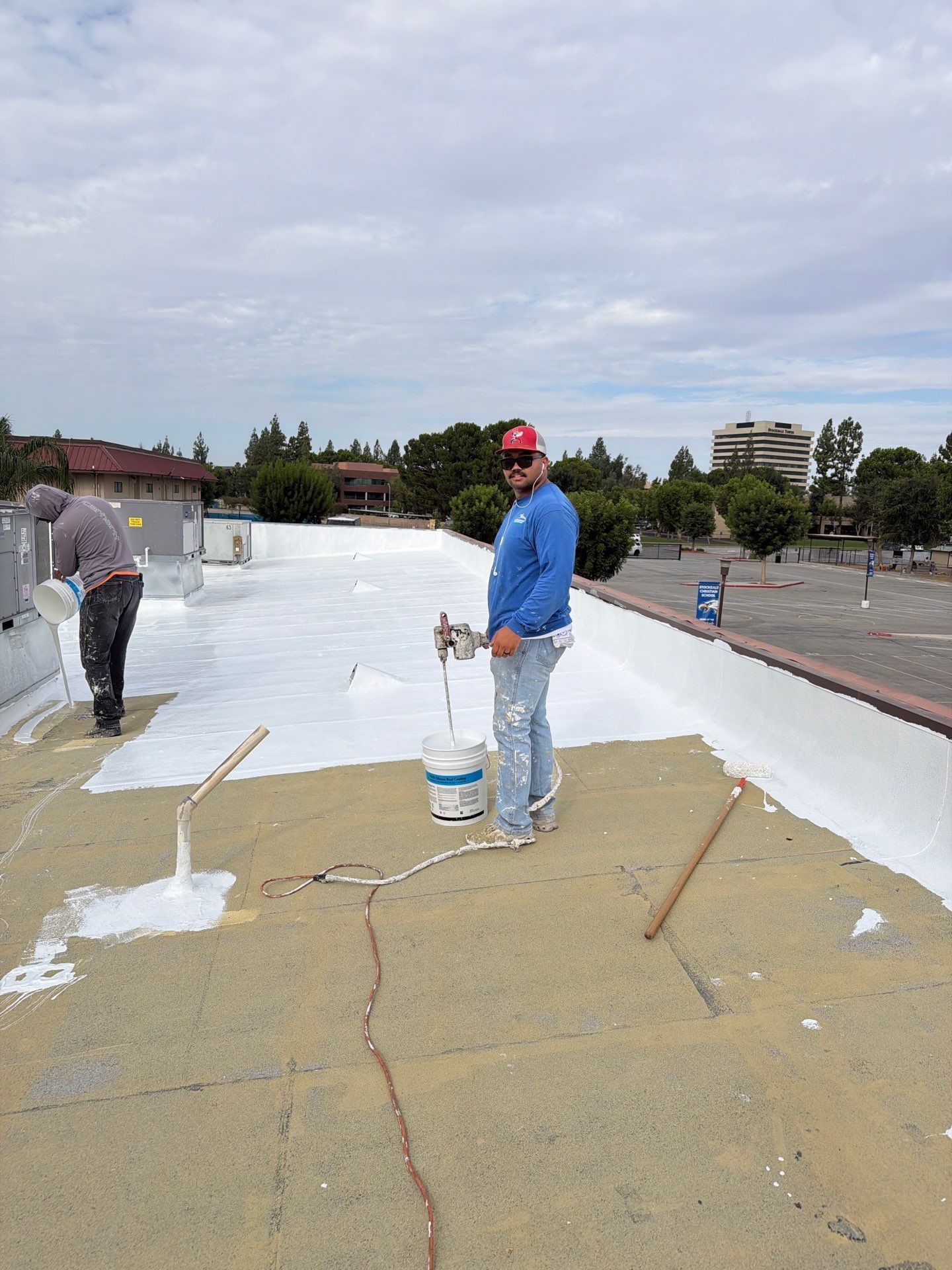 Workers repainting a rooftop deck white, with one person rolling paint under a cloudy sky