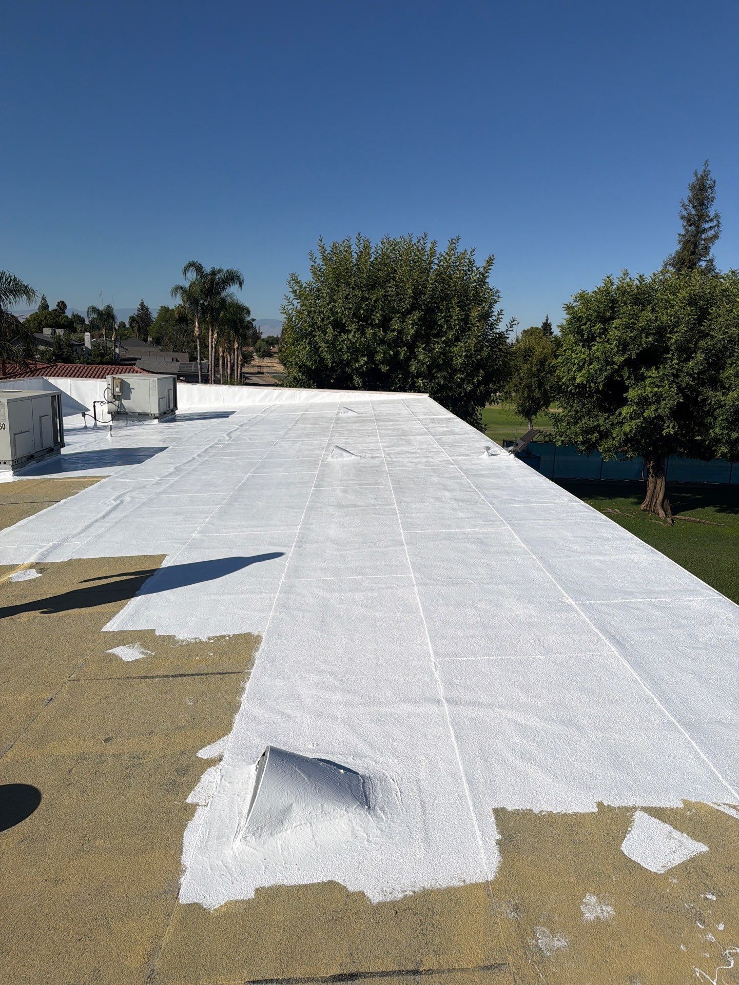 Flat white roof under repair with patches and trees in the background