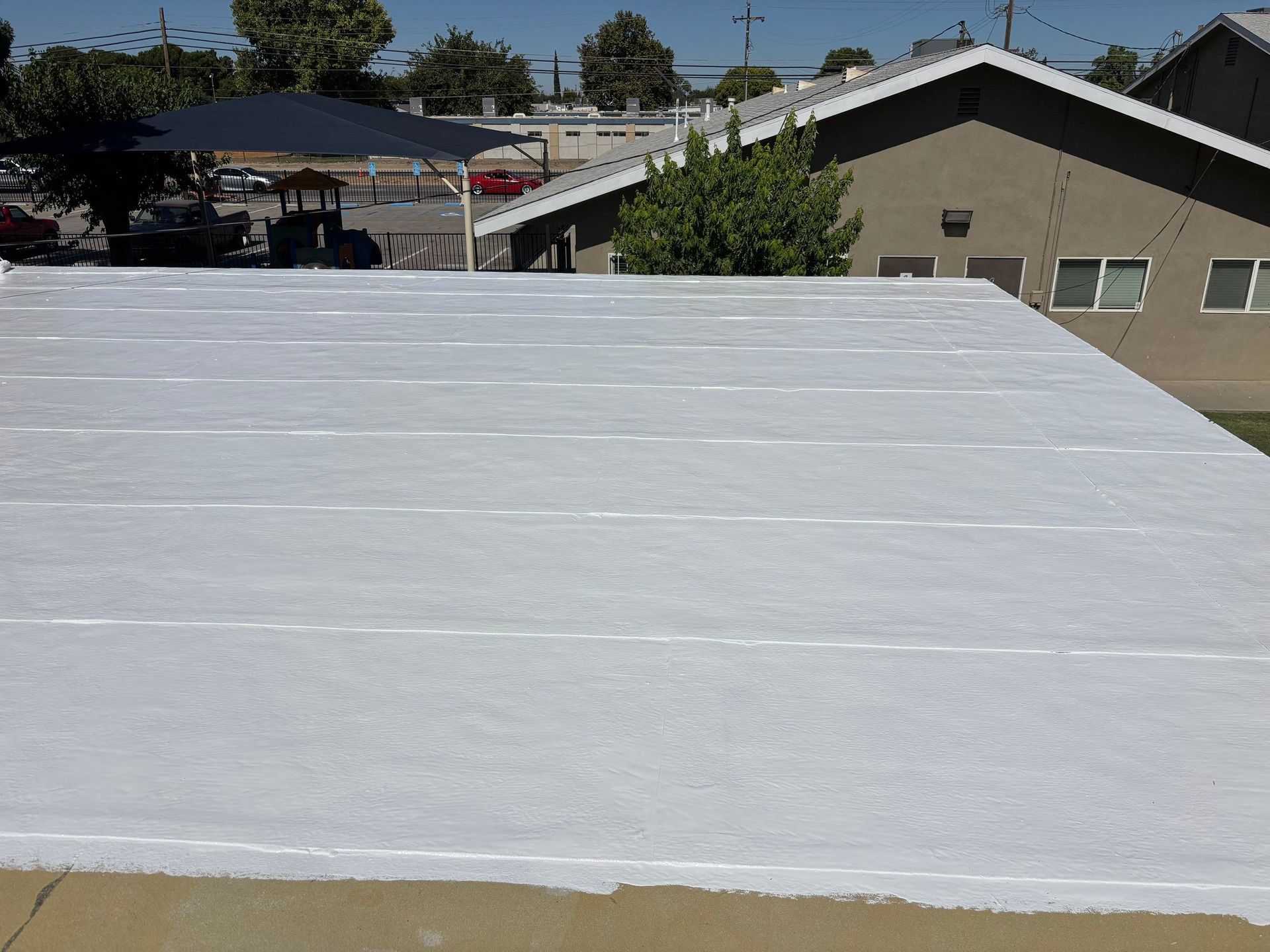 White flat rooftop in the foreground with houses, trees, and a clear blue sky in the background