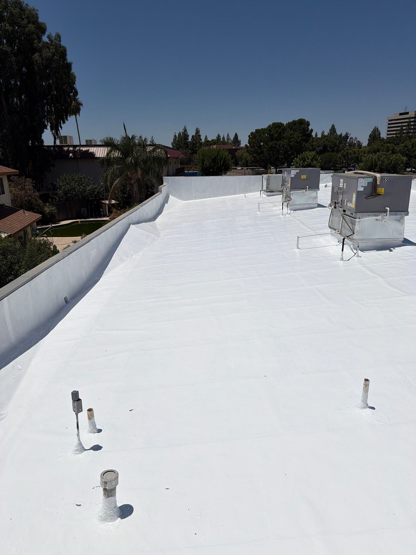 White rooftop with HVAC units and vents under a clear blue sky