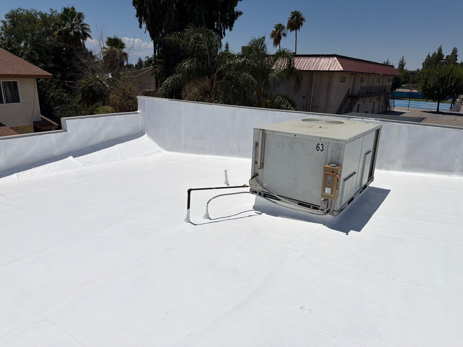 White rooftop with a gray metal box unit and distant trees and houses under a clear sky