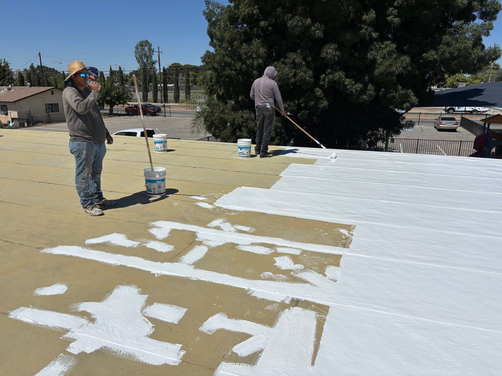 Workers painting a flat roof white with rollers on a sunny day