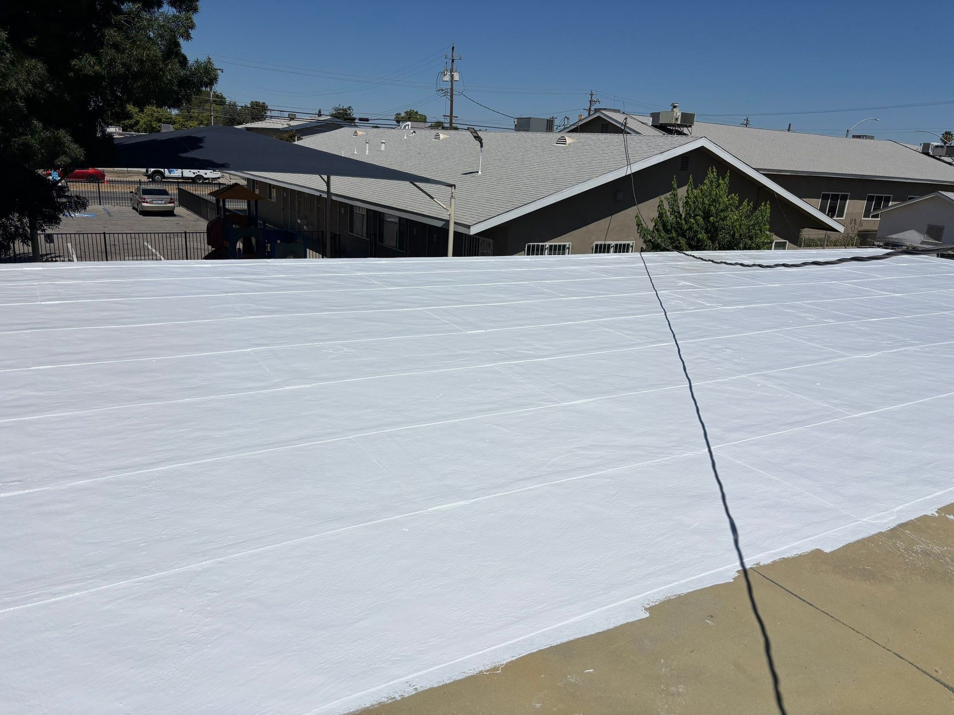 White roof membrane on a low-rise building under a clear blue sky, viewed from above.