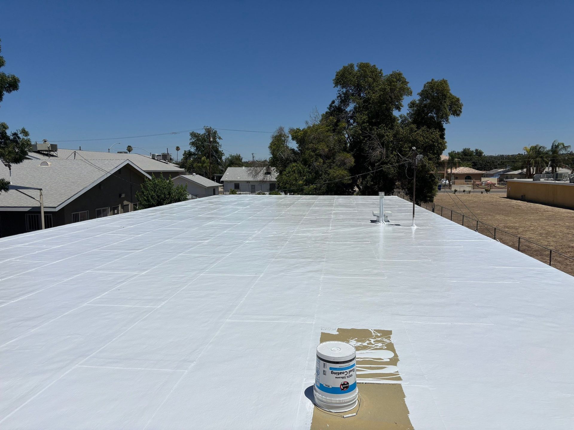 White roof coating with a paint bucket on a flat rooftop under a clear blue sky