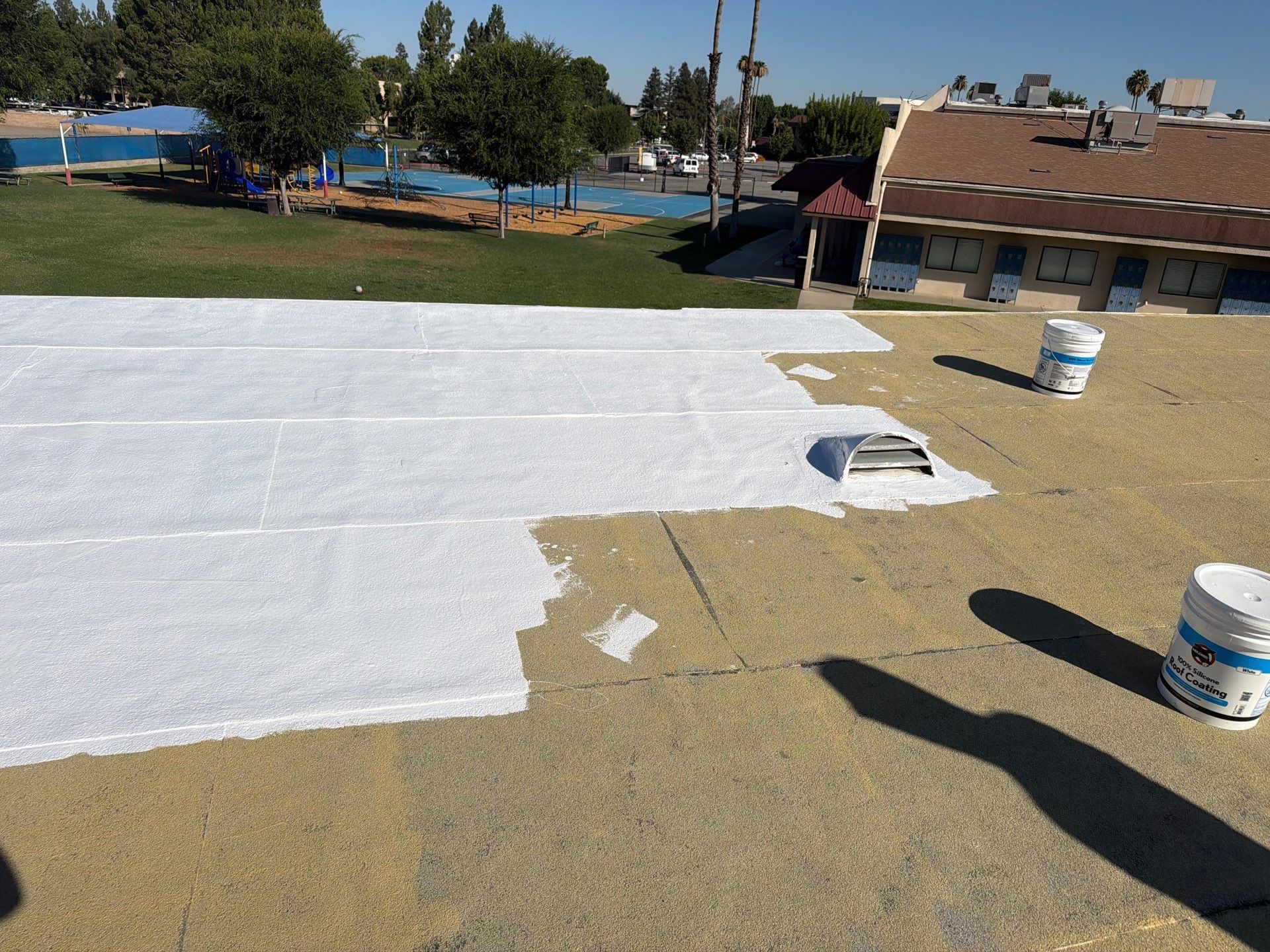 White roof coating being rolled onto a flat rooftop, with paint buckets nearby.