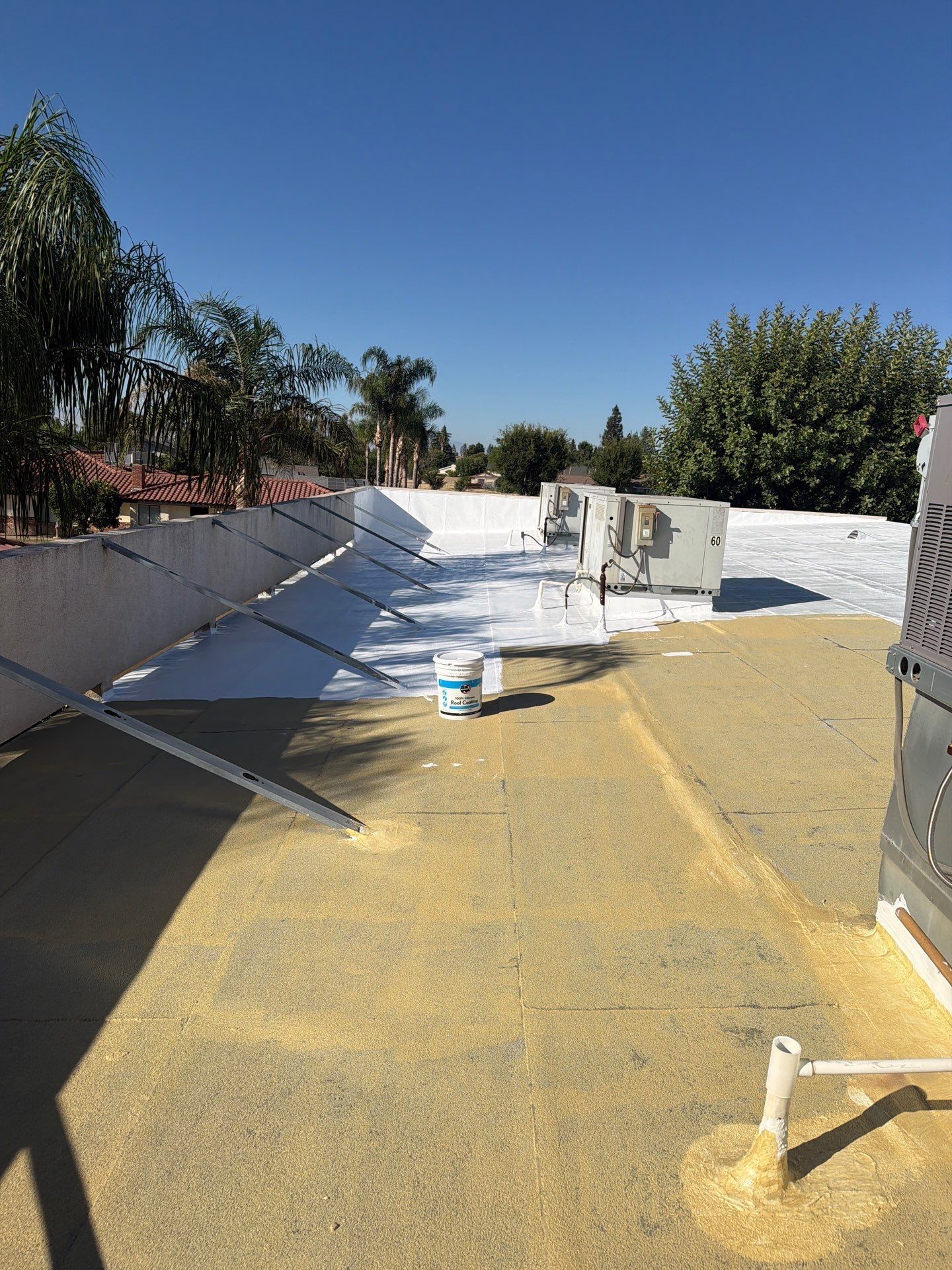 Flat rooftop with HVAC units, white parapet walls, and yellow roofing under a clear blue sky.