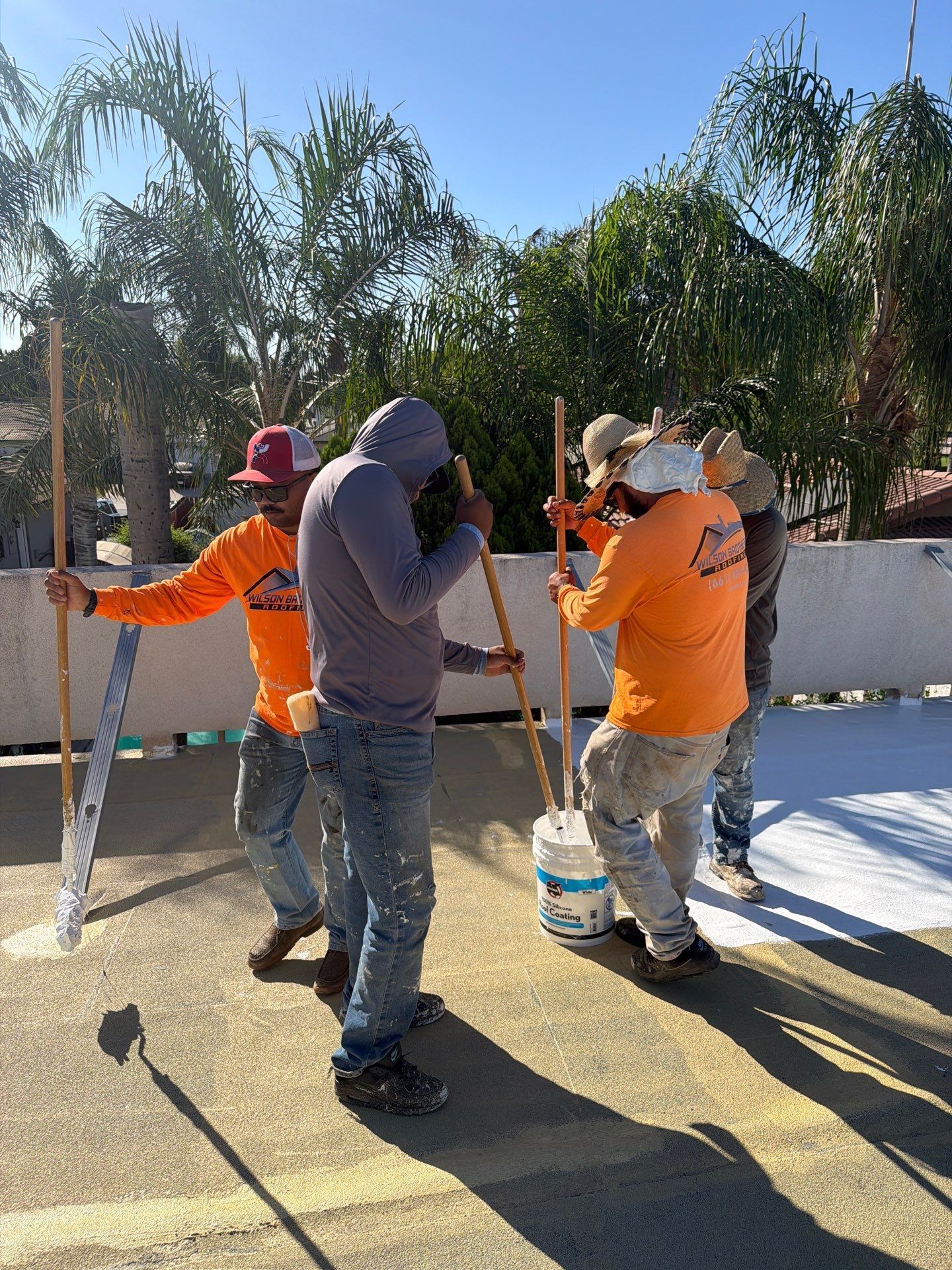 Three workers painting a white fence outdoors on a sunny day.