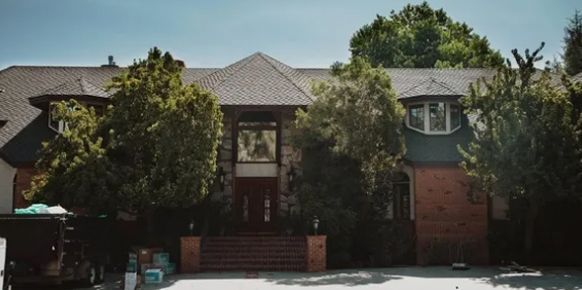 Suburban house with brick columns, large windows, and trees in front.