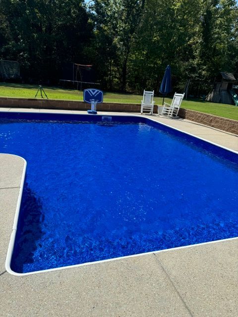 A large blue swimming pool with a basketball hoop in the backyard.