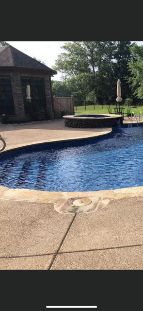 A large swimming pool with a patio in front of a house.
