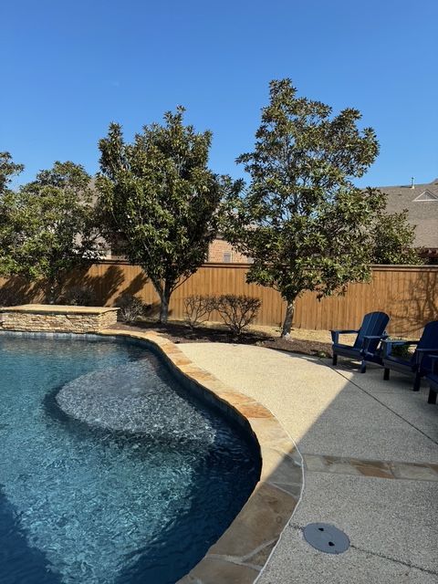 A swimming pool surrounded by chairs and trees on a sunny day