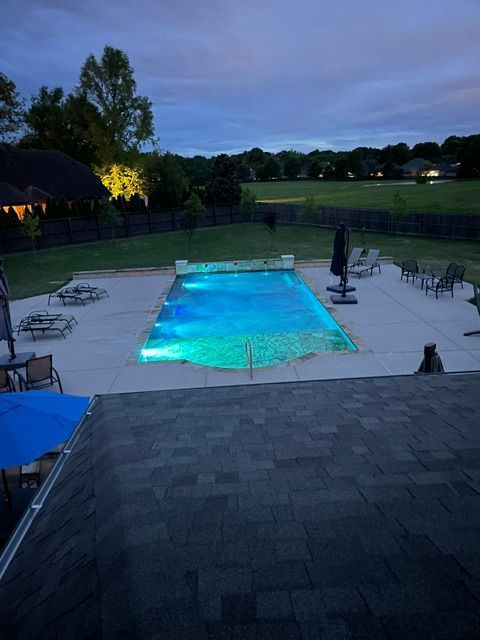 A large swimming pool is lit up at night in a backyard.