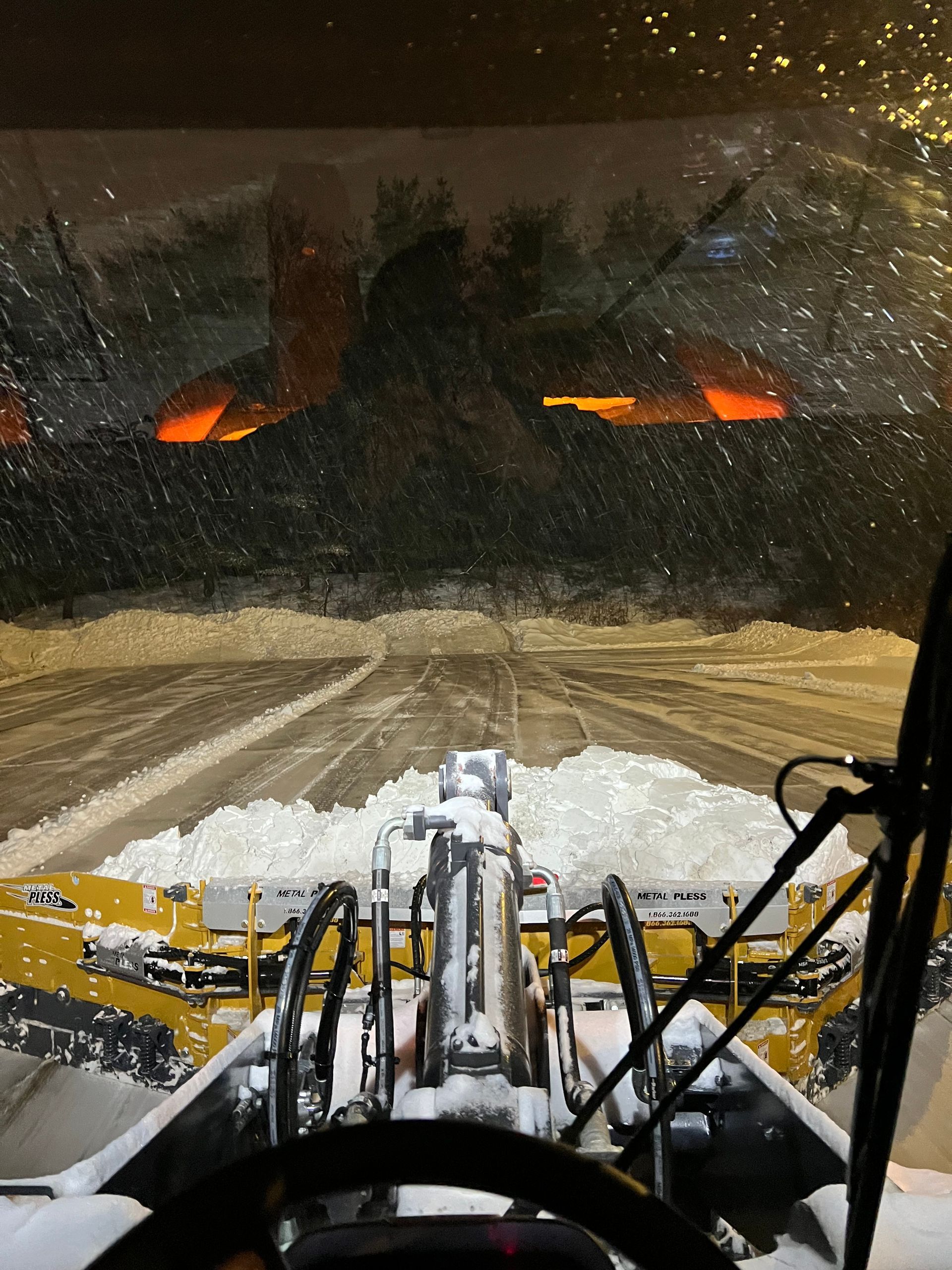 A person is driving a snow plow on a snowy road at night