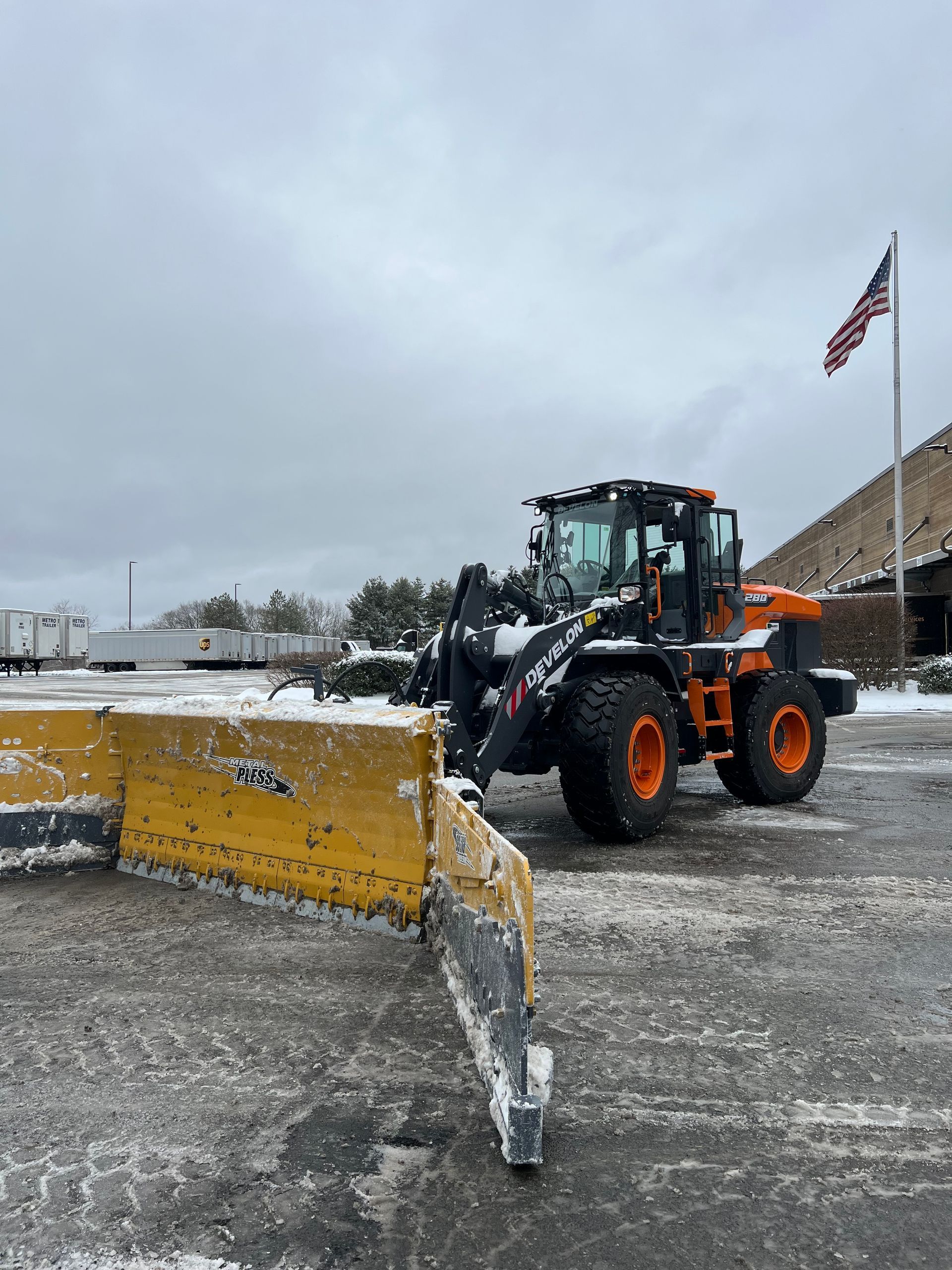 A snow plow is parked in a parking lot next to an american flag.