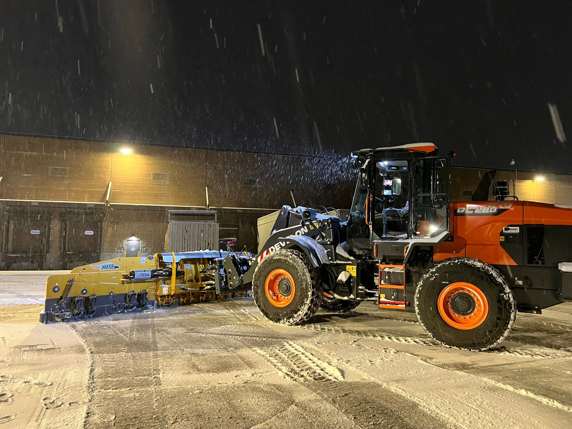 A tractor is plowing snow in a parking lot at night.