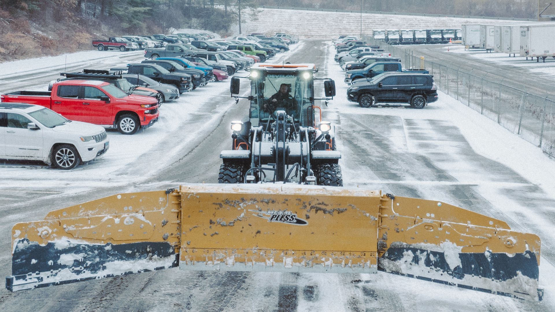 A snow plow is clearing snow from a parking lot.